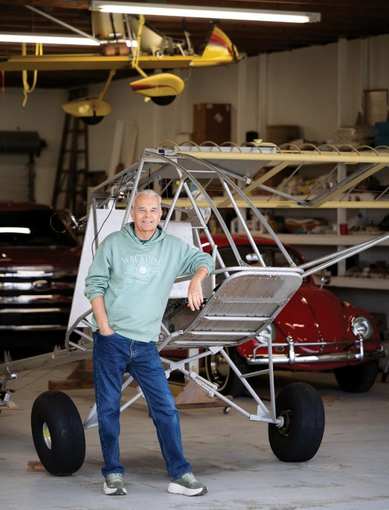 The Drifter ultralight is suspended from the ceiling of Roy Pinner’s hangar ahead of its final trip to the EAA Aviation Museum, while Pinner leans against his newest project, a STOL. Photo by Steven Martine
